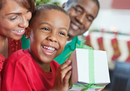 Happy little boy opening a Christmas present with his parents